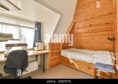 Interior of bedroom with bed placed against wooden wall near table with sewing machine and table in light apartment Stock Photo