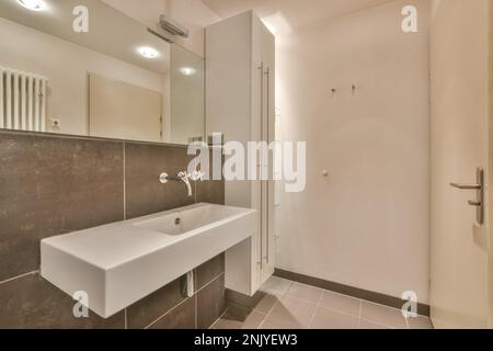 White ceramic sink under mirror placed near cabinet against tiled wall in light bathroom interior Stock Photo