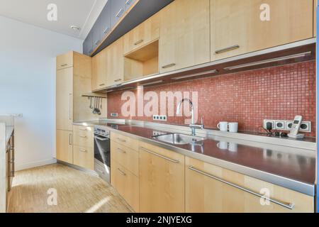 Interior design of modern kitchen with wooden cupboards backsplash made of red mosaic small square tile and sink on counter near oven with electric st Stock Photo