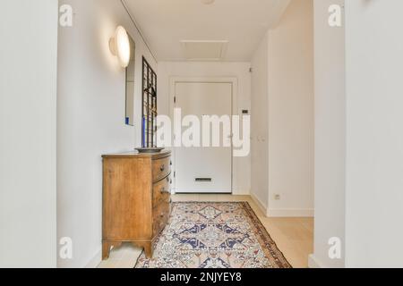 Interior design of light hallway with white walls entrance door and wooden commode placed on carpet under glowing lamp near mirror Stock Photo