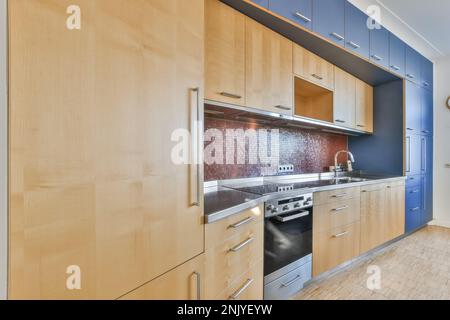Interior design of modern kitchen with wooden cupboards backsplash made of red mosaic small square tile and sink on counter near oven with electric st Stock Photo
