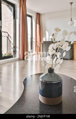 Glass vase with dry branches of plant placed on table against window with curtains in light apartment Stock Photo