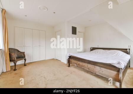 Interior of light bedroom with comfortable double bed with white bedclothes and built in wardrobe near antique armchair Stock Photo