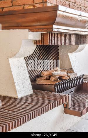 Interior design of fireplace surrounded with white stone under brick range hood with wooden mantel shelf on gray floor tile in house in traditional st Stock Photo