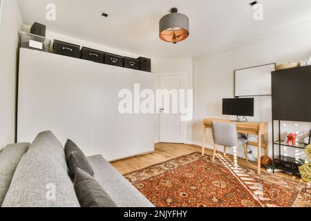 Interior design of modern room with gray couch near white wardrobe against wooden table with desktop placed on carpet Stock Photo