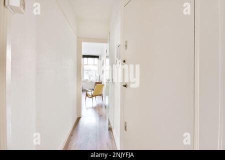 Interior design of narrow hallway with white walls and wooden parquet leading to room with yellow armchair Stock Photo