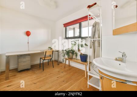 Interior design of modern light studio apartment with wooden floor white walls and sink under mirror near rack and small windows against table decorat Stock Photo