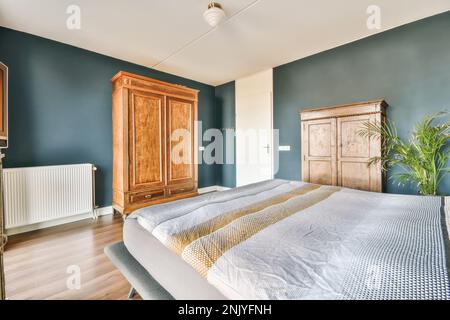 Interior design of modern bedroom furnished with bed placed near bedside table and wooden wardrobe with potted plant Stock Photo