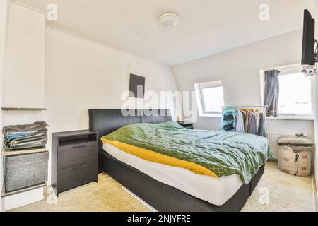 Interior design of modern bedroom with king size bed with black leather headboard and bedside cabinets under black picture on white wall Stock Photo