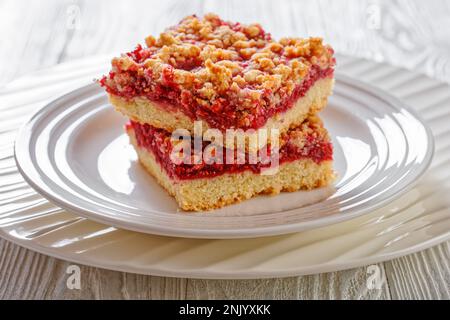 Raspberry Crumble Bars on white plate on white wood table, horizontal view from above, close-up Stock Photo
