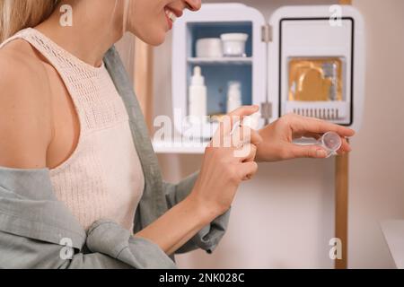 Woman taking cosmetic product from mini fridge indoors, closeup Stock Photo