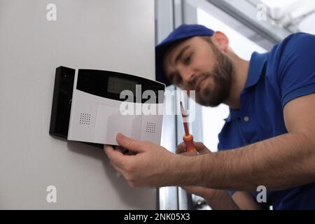 Man installing home security system on white wall in room Stock Photo