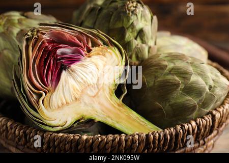 Cut and whole fresh raw artichokes in wicker basket, closeup Stock Photo