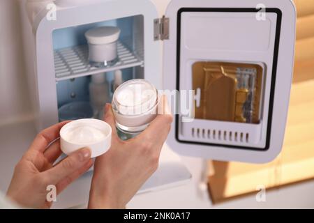 Woman taking cosmetic product from mini fridge indoors, closeup Stock Photo