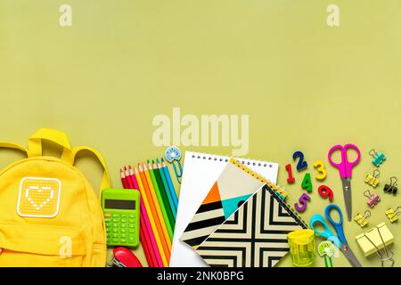 Back to school, education concept Yellow backpack with school supplies - notebook, pens, eraser rainbow, numbers isolated on green background Top view Stock Photo