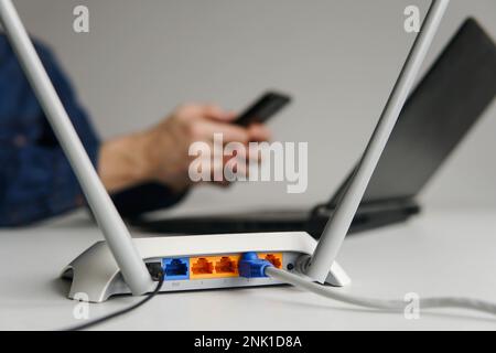 Wireless high speed wifi router on the table. Man using smartphone on the background Stock Photo