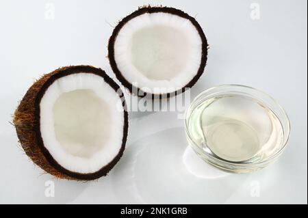 Coconut oil in a glass cup with split coconuts in the background Stock Photo
