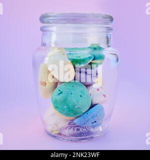Glass jar, beach stones or rocks on table in studio isolated on a purple background. Beauty, art and variety of colorful pebbles in bottle collected Stock Photo