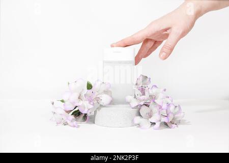 The girl takes a bottle of clear micellar water. Transparent micellar water in a white plastic bottle on a podium pedestal on white gray background wi Stock Photo