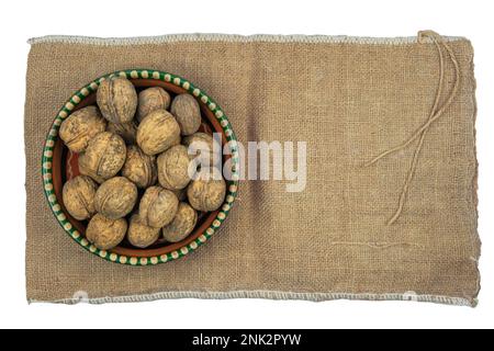 Walnuts in the shell in a clay bowl on the background of burlap. Isolated on white background. Top view. Stock Photo