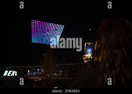 (230223) -- BUSAN, Feb. 23, 2023 (Xinhua) -- A woman records videos of a drone light show over the Busan Exhibition & Convention Center (BEXCO) in Busan, South Korea, Feb. 23, 2023.  As part of the Drone Show Korea 2023 held in the city on Thursday, 500 drones put on a light show at night over the exhibition center. The exhibition of unmanned aerial vehicles (UAV) kicked off here to showcase latest technologies and models and to discuss the future of the industry. (Xinhua/Wang Yiliang) Stock Photo