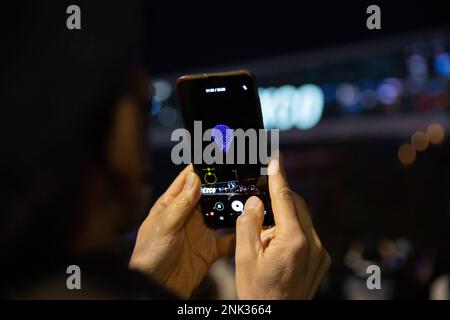 (230223) -- BUSAN, Feb. 23, 2023 (Xinhua) -- A man records videos of a drone light show over the Busan Exhibition & Convention Center (BEXCO) in Busan, South Korea, Feb. 23, 2023.  As part of the Drone Show Korea 2023 held in the city on Thursday, 500 drones put on a light show at night over the exhibition center. The exhibition of unmanned aerial vehicles (UAV) kicked off here to showcase latest technologies and models and to discuss the future of the industry. (Xinhua/Wang Yiliang) Stock Photo