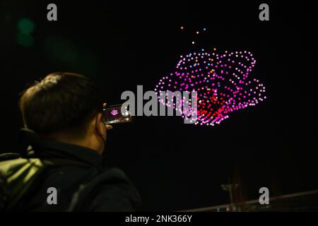 (230223) -- BUSAN, Feb. 23, 2023 (Xinhua) -- A man records videos of a drone light show over the Busan Exhibition & Convention Center (BEXCO) in Busan, South Korea, Feb. 23, 2023.  As part of the Drone Show Korea 2023 held in the city on Thursday, 500 drones put on a light show at night over the exhibition center. The exhibition of unmanned aerial vehicles (UAV) kicked off here to showcase latest technologies and models and to discuss the future of the industry. (Xinhua/Wang Yiliang) Stock Photo