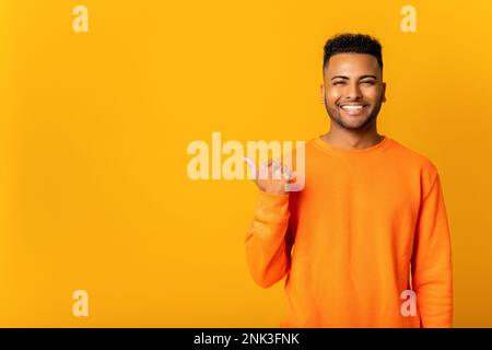 Smiling cheerful young man points aside and looking at the camera with cheerful wide toothy smile, guy presenting novelty, advertising, isolated on yellow wall Stock Photo