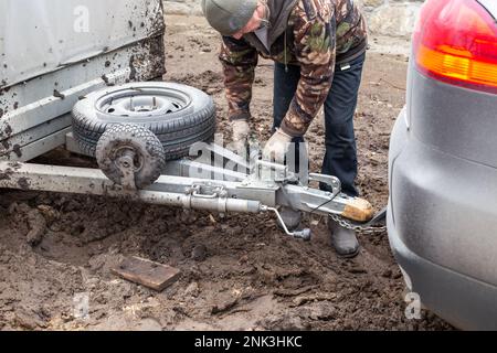 A man checking the hitch mechanism on a car trailer in bad weather. Stock Photo