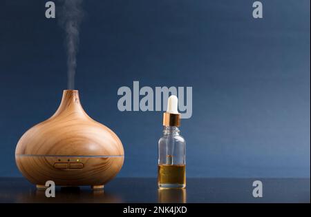 wooden air freshener with steam of natural essences with oil dispenser, brown table with blue background Stock Photo