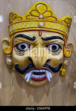 Handmade colorful tribal look of Ravan face mask souvenir hanging on plain black background. Selective focus on object. Stock Photo