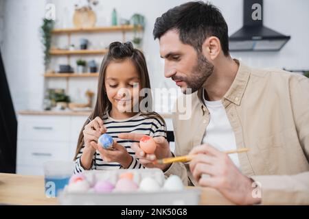 Smiling girl painting Easter eggs with father in kitchen Stock Photo