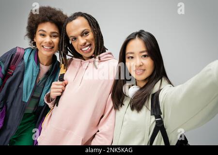 joyful multicultural students in hoodies and jacket posing and looking at camera isolated on grey,stock image Stock Photo