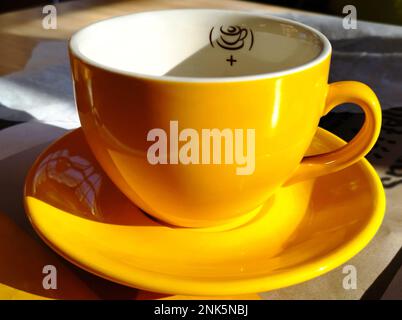 empty yellow porcelain cappuccino cup or mug in closeup view. shiny reflective smooth surface. strong shadows. coffee consumption concept. Stock Photo