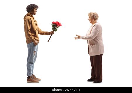 Full length profile shot of an african american man smiling and giving a bunch of red roses to an elderly woman isolated on white background Stock Photo
