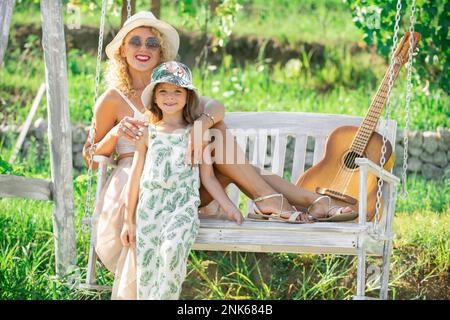 Happy mother and child swinging. Young mother with little kid son sitting on swing in summer park. Mothers day. Happiness, loving family and Stock Photo
