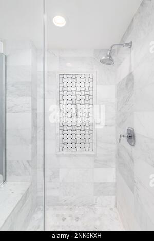 A shower with marble subway and hexagon tiles, an interlocking tile pattern on the wall, bench seat, and chrome showerhead. Stock Photo