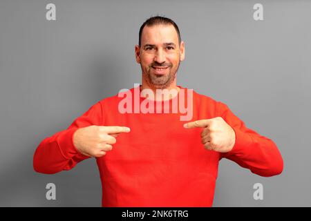 Bearded hispanic man wearing a red sweater pointing to himself proudly isolated on gray background. He is satisfied with his work, he feels effective Stock Photo