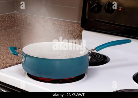 Horizontal shot of a blue pot on a stove top with steam rising from boiling water. Stock Photo