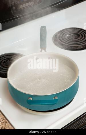 Vertical close-up shot of a blue pot on a stove top with steam rising from  boiling water. Stock Photo