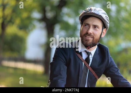 Handsome male businessman in protective helmet commuting at daytime. Portrait of young happy man in stylish suit and tie smiling, while looking around Stock Photo