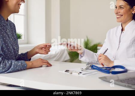 Caucasian woman doctor in white coat transmits paper with recommendation for treatment sits at table Stock Photo