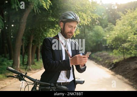 Concentrated male entrepreneur surfing internet on smartphone, while searching way to job outdoors. Front view of bearded man in suit checking mobile Stock Photo