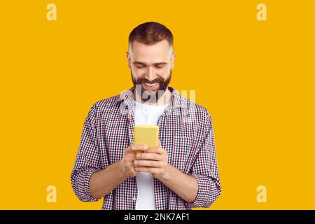 Happy young man in casual shirt looking at his mobile phone, text messaging and smiling Stock Photo