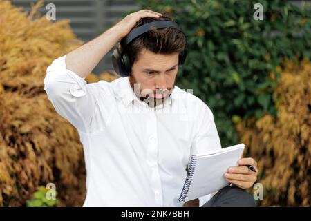 Puzzled businessman scratching head, having hard decision, while looking at notepad outside. Portrait of confused man having doubt, difficulties, hand Stock Photo