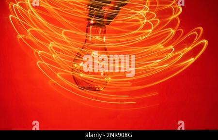 Christmas accessory-garland of LED light bulbs in a glass flask on a red abstract background. The hand with the flask makes oscillatory movements, lea Stock Photo