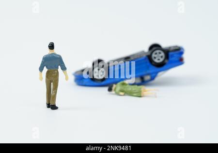 On a white background, a man who is walking towards a car overturned as a result of an accident and a woman lying down. Stock Photo