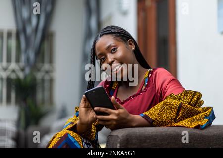 African Woman holding smartphone smiles at camera. Stock Photo