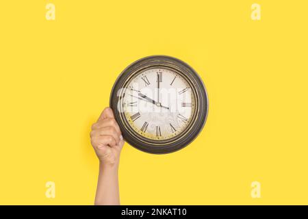 Woman hand holding a wall clock on a yellow background with copy space Stock Photo