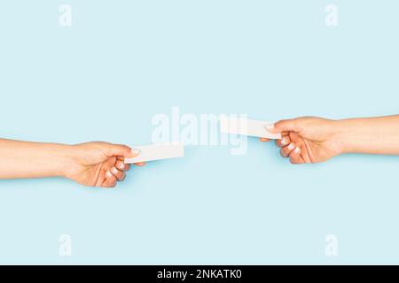 Women hands exchanging blank white personal cards on a light blue backgroud with copy space Stock Photo